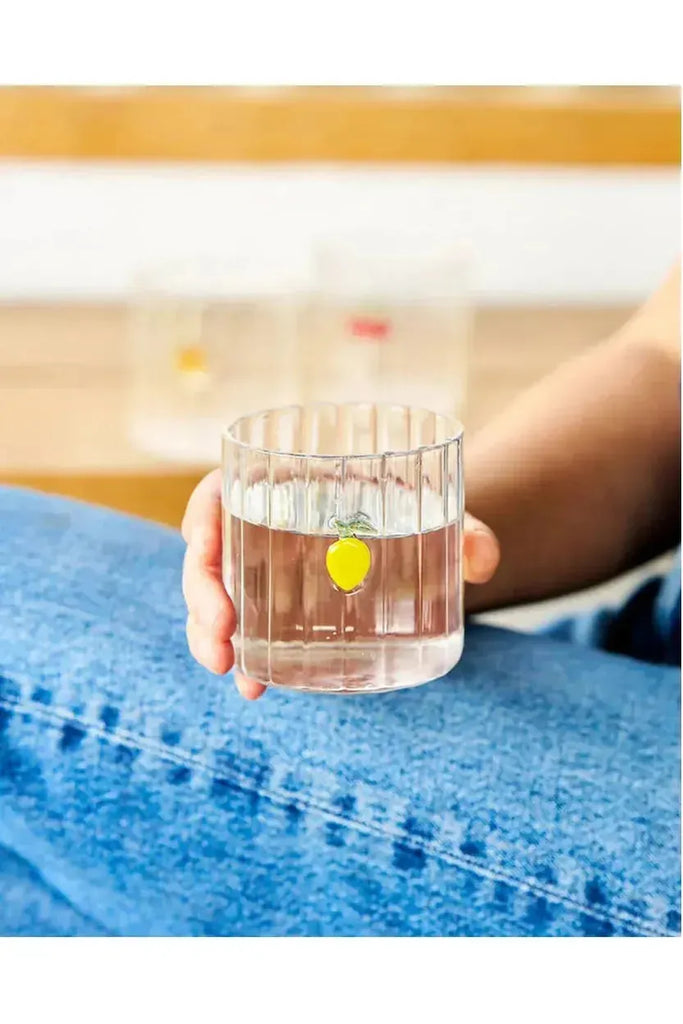Introducing the vibrant Robert Gordon Lemon Haven Glass Tumbler, beautifully etched with a cheerful lemon design, perfectly showcased in a hand holding refreshing, clear liquid.