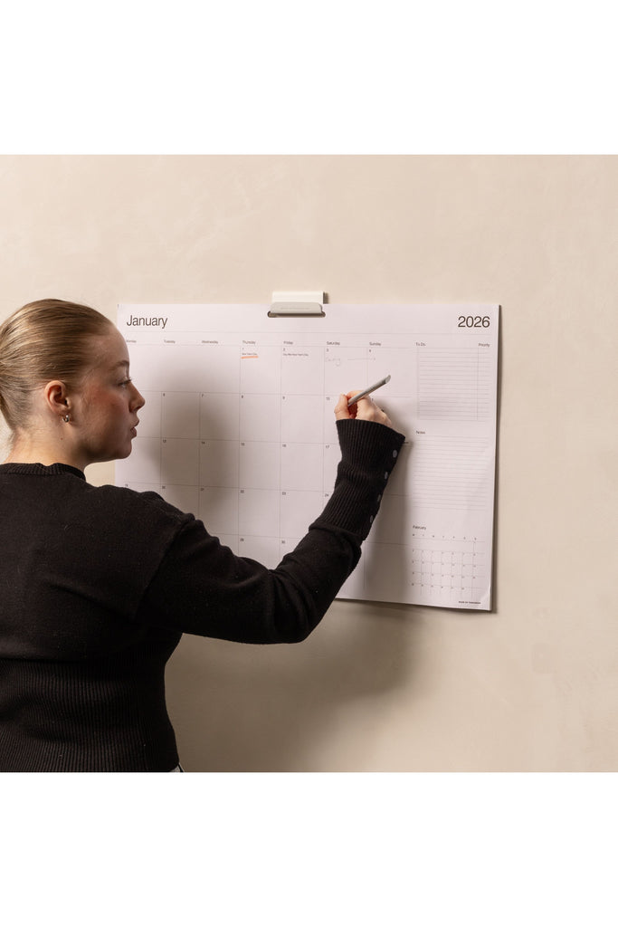 Made of Tomorrow 2026 Monthly Wall Planner. The image shows a Person writing on the calendar attached to a wall.