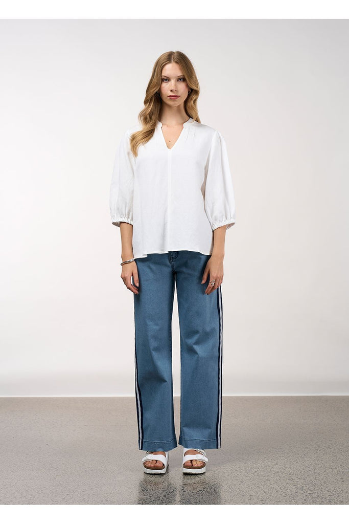 Woman wearing a white blouse and blue jeans against a plain background. Madly Sweetly Octave Top in White.