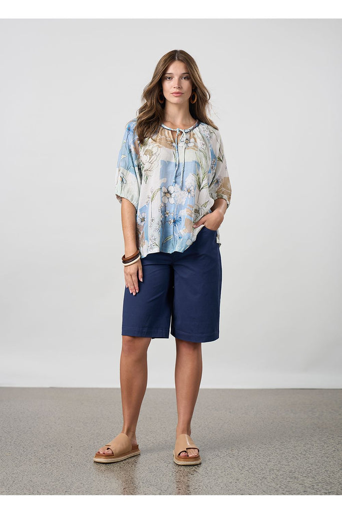 Woman wearing a floral top and navy shorts on a plain background. Madly Sweetly Ratio Shorts in Navy.