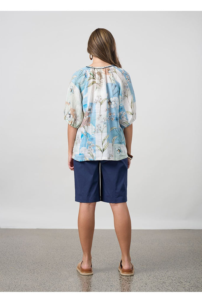 Woman wearing a floral top and navy shorts on a plain background. Madly Sweetly Ratio Shorts in Navy.