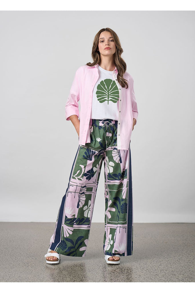 Woman wearing a white tee pink jacket and floral pants against a plain background. Madly Sweetly Silhouette Pant.