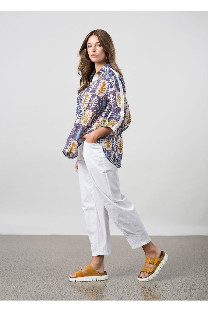 Woman wearing a floral shirt and white pants standing against a plain background. Madly Sweetly Ratio Pant in White.