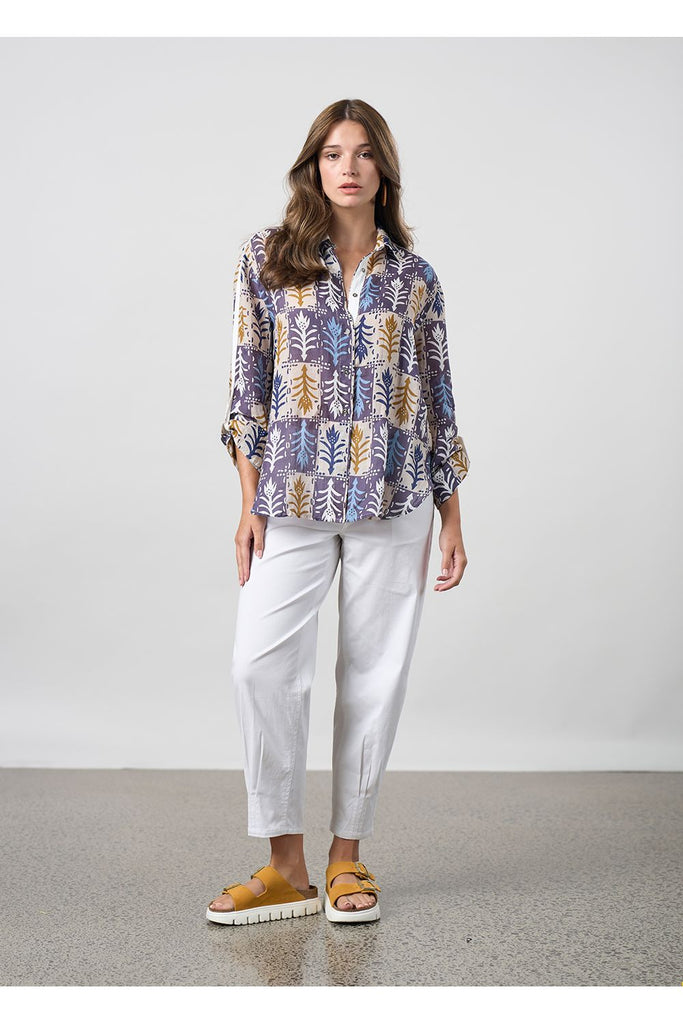 Woman wearing a floral shirt and white pants standing against a plain background. Madly Sweetly Ratio Pant in White.