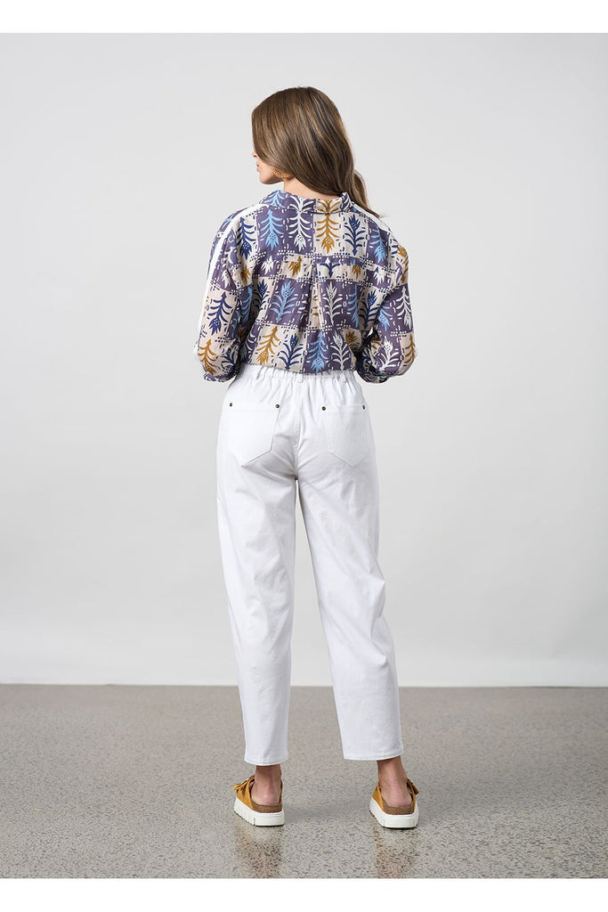 Woman wearing a floral shirt and white pants standing against a plain background. Madly Sweetly Ratio Pant in White.