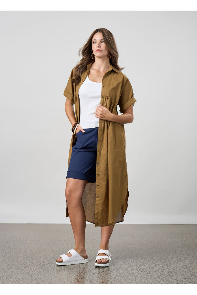 Woman wearing a long brown shirt over a white top and blue shorts on a plain background. Madly Sweetly Ratio Shorts in Navy.