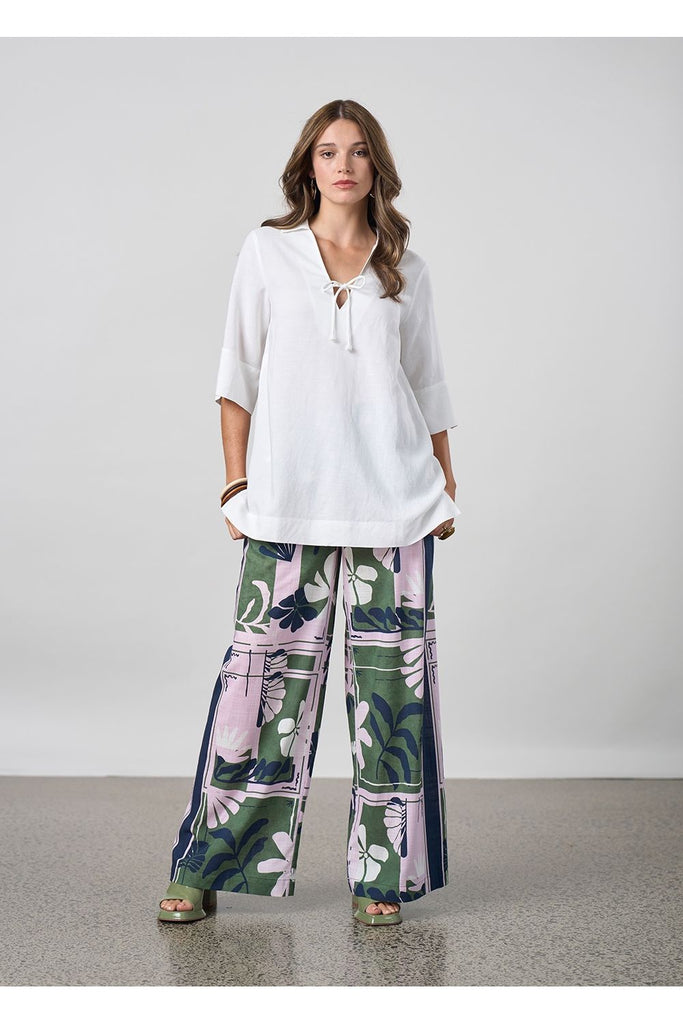 Woman wearing a white blouse and floral pants against a plain background. Madly Sweetly Silhouette Pant.