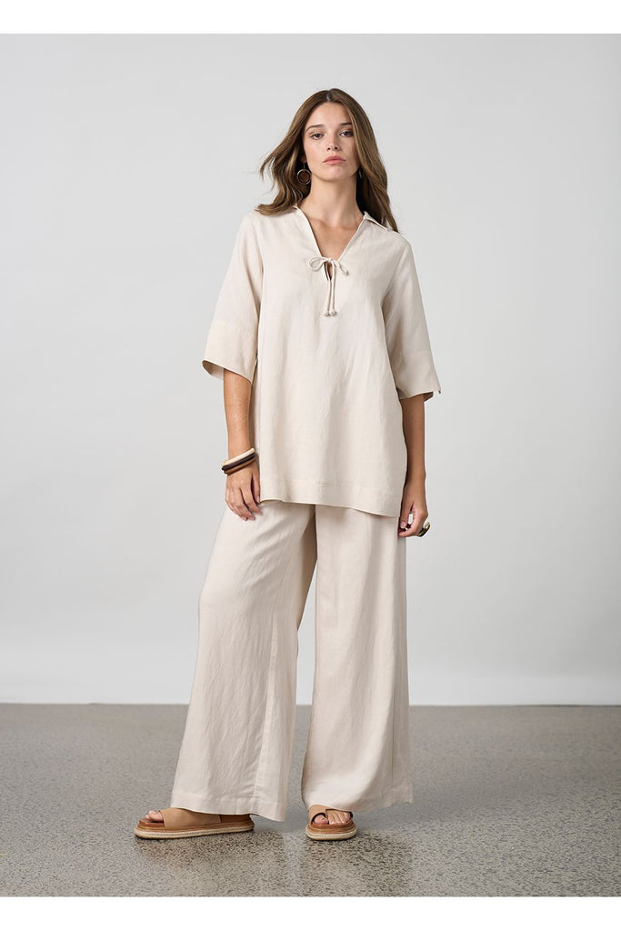 Woman wearing a beige top and beige pants against a plain background. Madly Sweetly Eclipse Pant in Chalk.