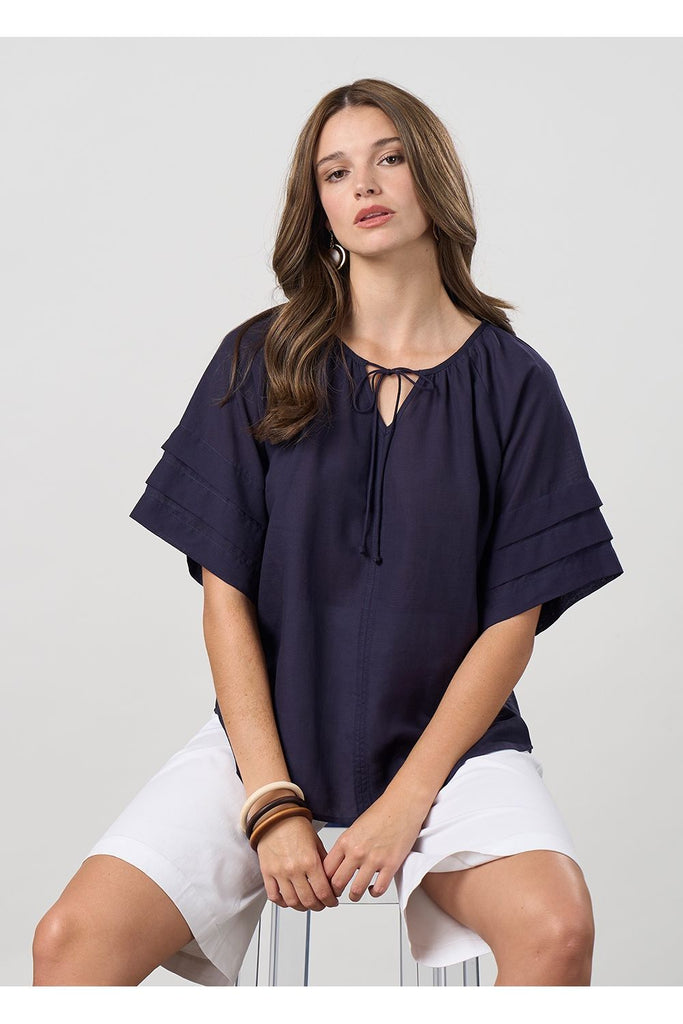 Woman wearing a navy blue blouse and white shorts on a light grey background. Madly Sweetly Parallel Top in Navy.