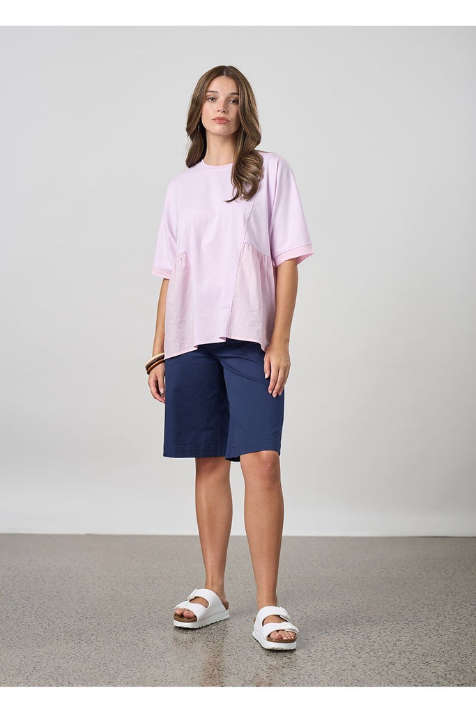 Woman wearing a pink top and navy shorts on a plain background. Madly Sweetly Ratio Shorts in Navy.