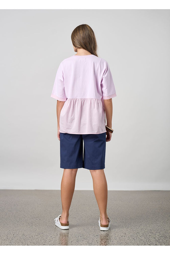 Woman wearing a pink top and navy shorts on a plain background. Madly Sweetly Ratio Shorts in Navy.