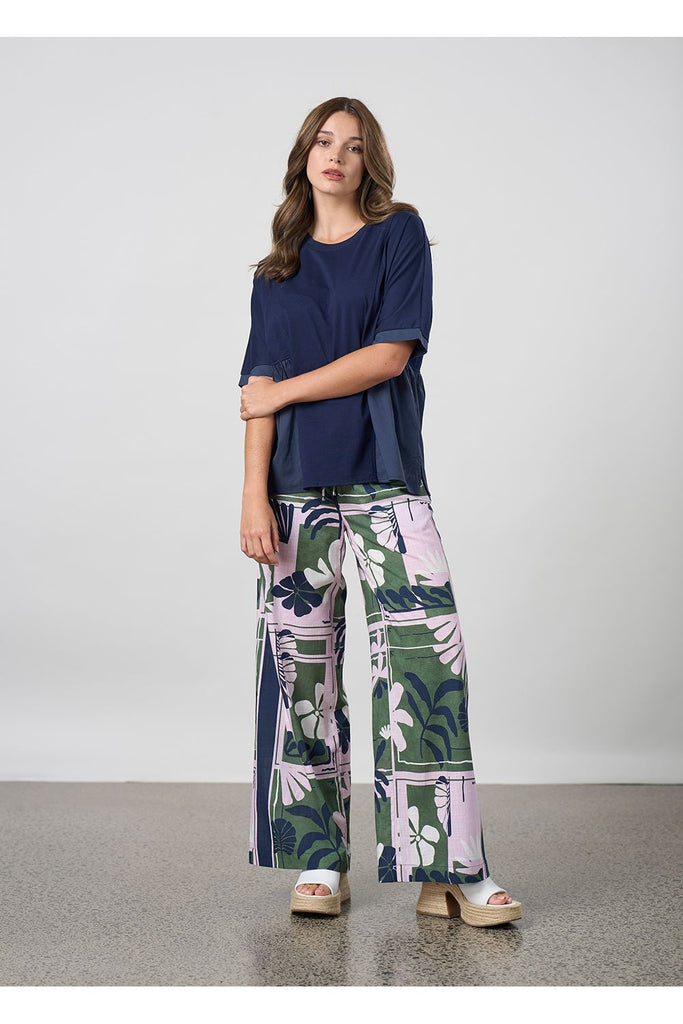 Woman wearing a navy blouse and floral pants against a plain background. Madly Sweetly Silhouette Pant.