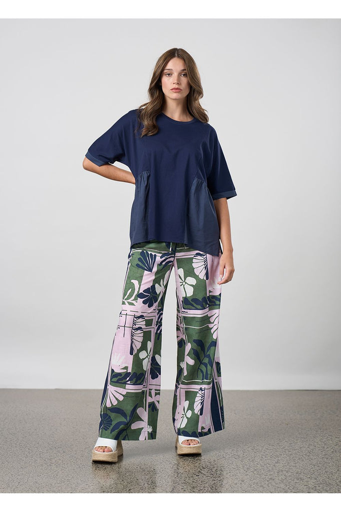Woman wearing a navy  blouse and floral pants against a plain background. Madly Sweetly Silhouette Pant.