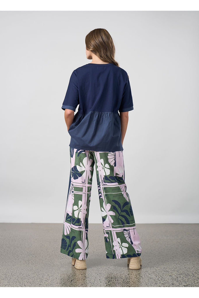 Woman wearing a navy blouse and floral pants against a plain background. Madly Sweetly Silhouette Pant.