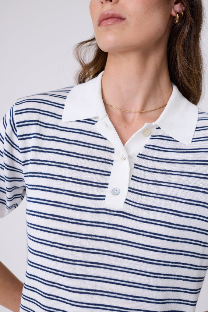 Woman wearing a striped polo shirt on a plain background. Marlow Chime Knit Polo Shirt in indigo Stripe.