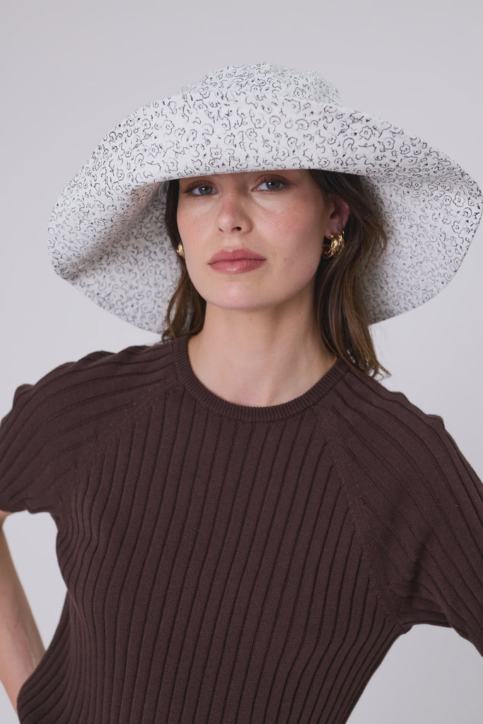 Woman wearing a floral sunhat and chocolate brown top against a plain background. Marlow Coastal Brim Hat and Wisp Knit Tee in Carob.