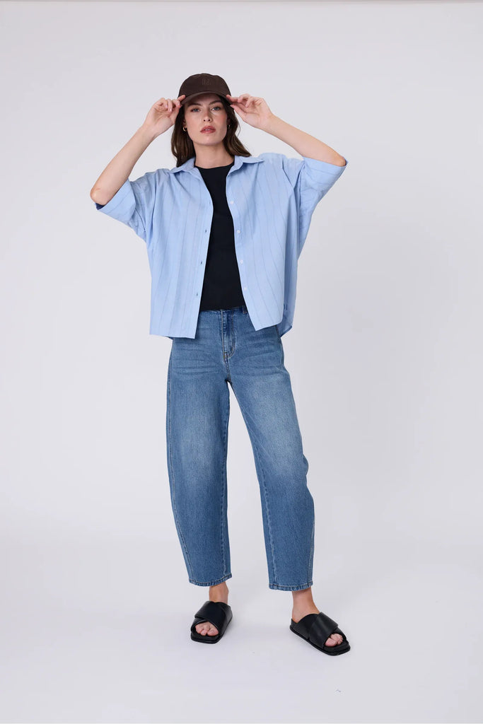 Woman wearing a brown cap and striped shirt and jeans against a plain background. Marlow Icon Linen Cap in carob.