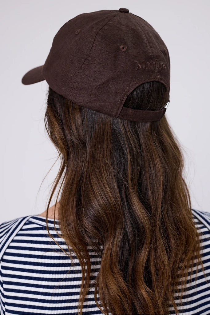 Woman wearing a brown cap and striped shirt against a plain background. Marlow Icon Linen Cap in carob.