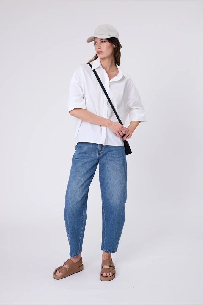 Woman wearing a light beige baseball cap and a white top on a plain background. Marlow Icon Linen Cap Natural.