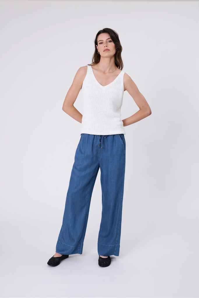 Woman wearing a white tank with blue denim pants on a white background. Marlow Marina Knit Tank in Chalk.