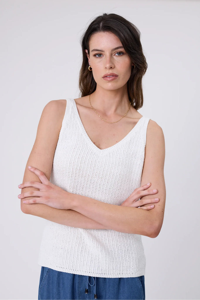 Woman wearing a white tank with blue denim pants on a white background. Marlow Marina Knit Tank in Chalk.