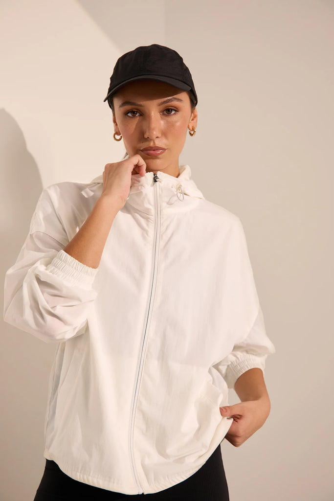 Person wearing a white windbreaker on a plain background. Motion Windbreaker in white from Marlow.
