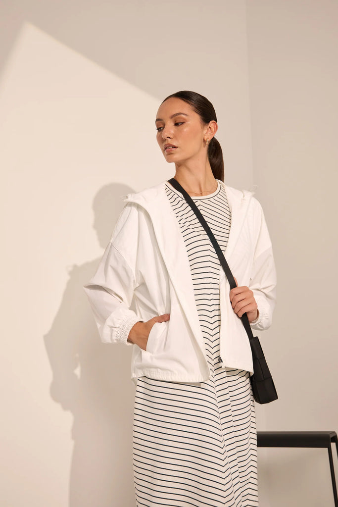 Person wearing a white windbreaker on a plain background. Motion Windbreaker in white from Marlow.