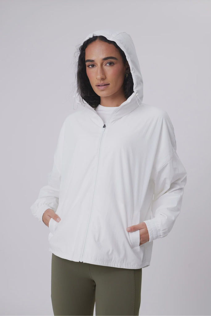 Person wearing a white windbreaker on a plain background. Motion Windbreaker in white from Marlow.