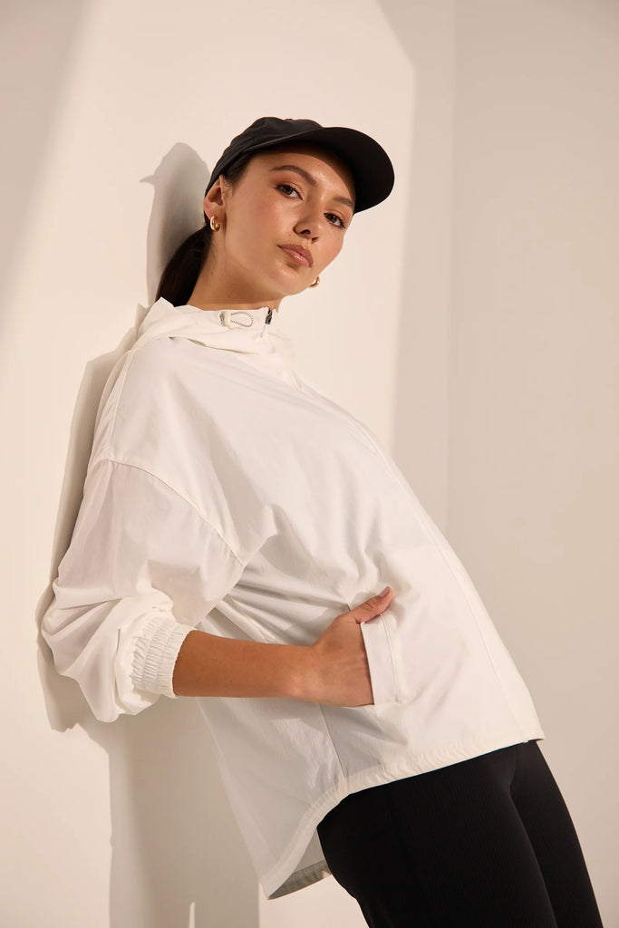 Person wearing a white windbreaker on a plain background. Motion Windbreaker in white from Marlow.