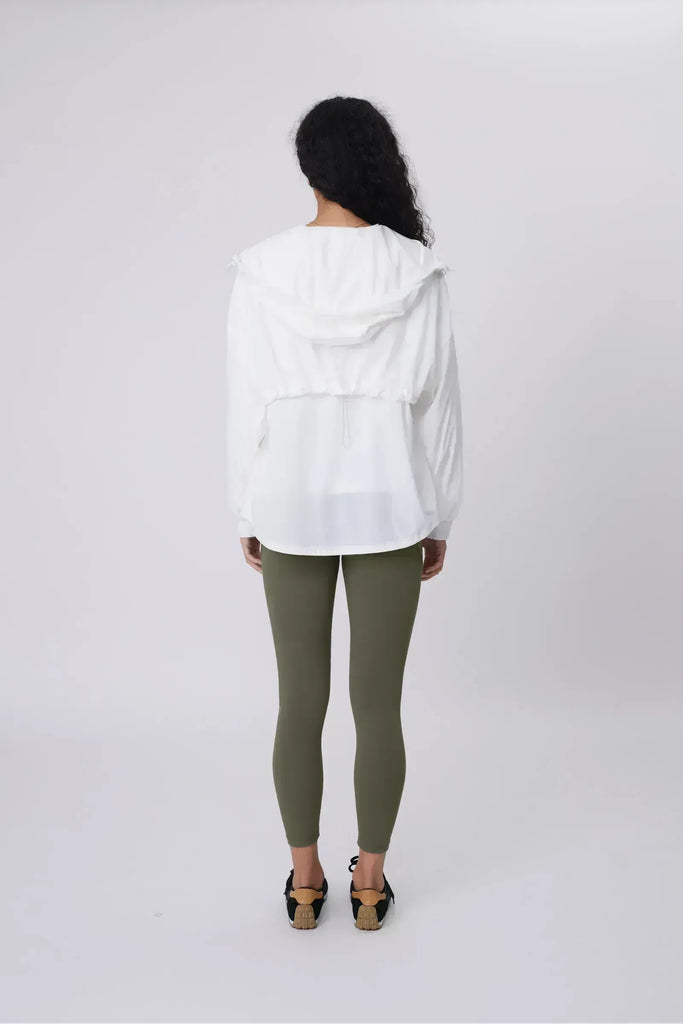 Person wearing a white windbreaker on a plain background. Motion Windbreaker in white from Marlow.