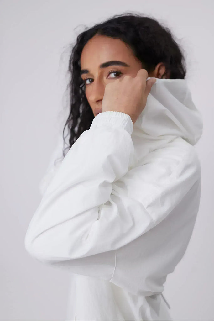 Person wearing a white windbreaker on a plain background. Motion Windbreaker in white from Marlow.