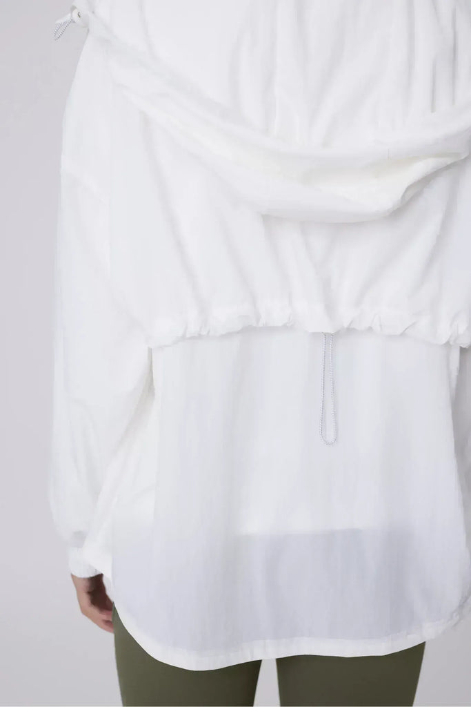 Person wearing a white windbreaker on a plain background. Motion Windbreaker in white from Marlow.