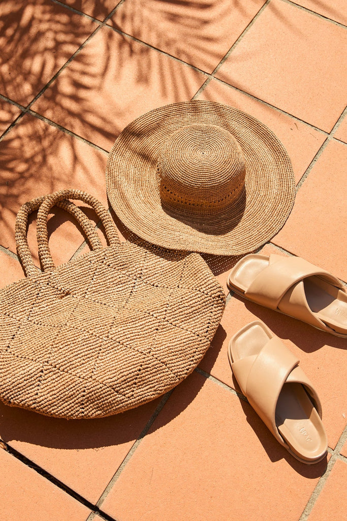 Wide brim sun hat , slides and raffia bag sitting on tiles outside. Marlow Mykonos Wide Brim Hat in Tea.