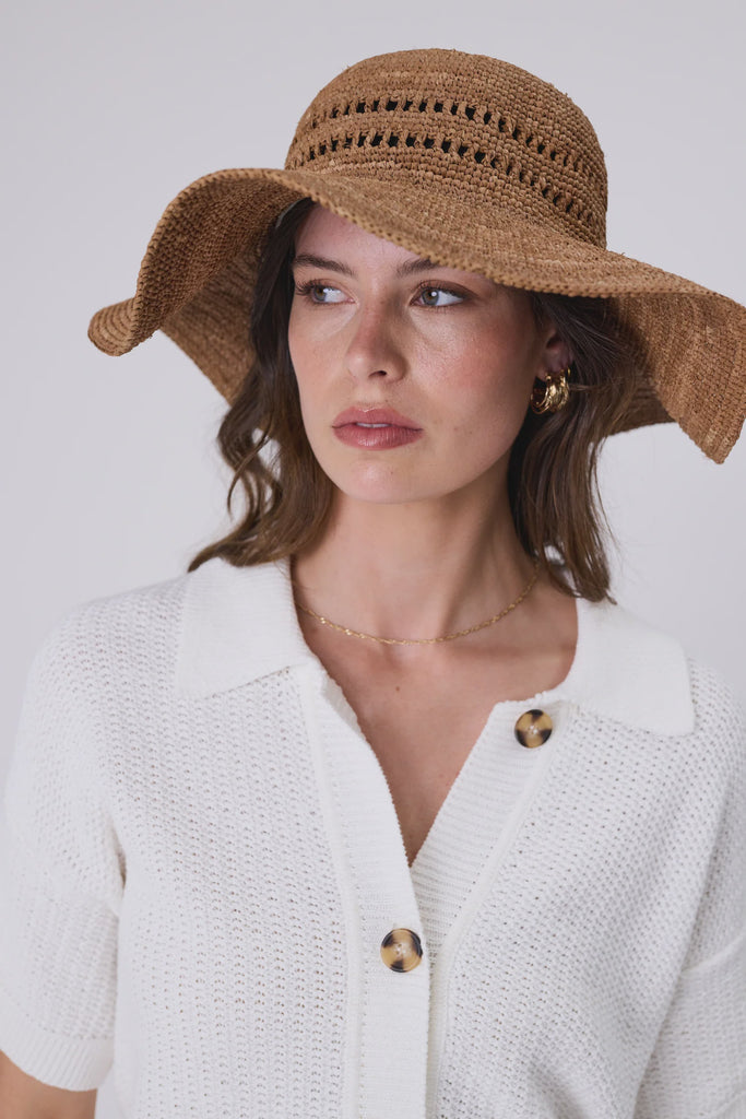 Woman wearing a wide brim sun hat and white top against a grey background. Marlow Mykonos Wide Brim Hat in Tea.