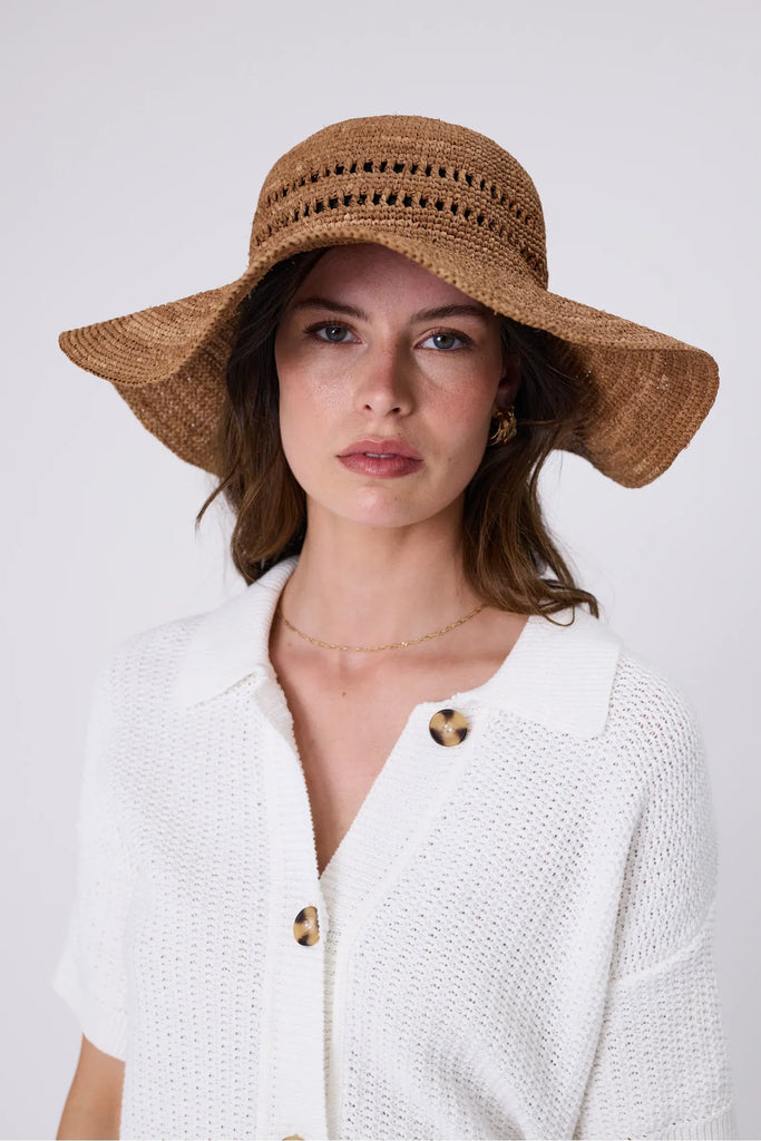 Woman wearing a wide brim sun hat and white top against a grey background. Marlow Mykonos Wide Brim Hat in Tea.