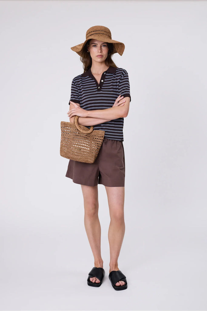 Woman wearing a wide brim sun hat and matching bag and stripe top against a grey background. Marlow Mykonos Wide Brim Hat in Tea.