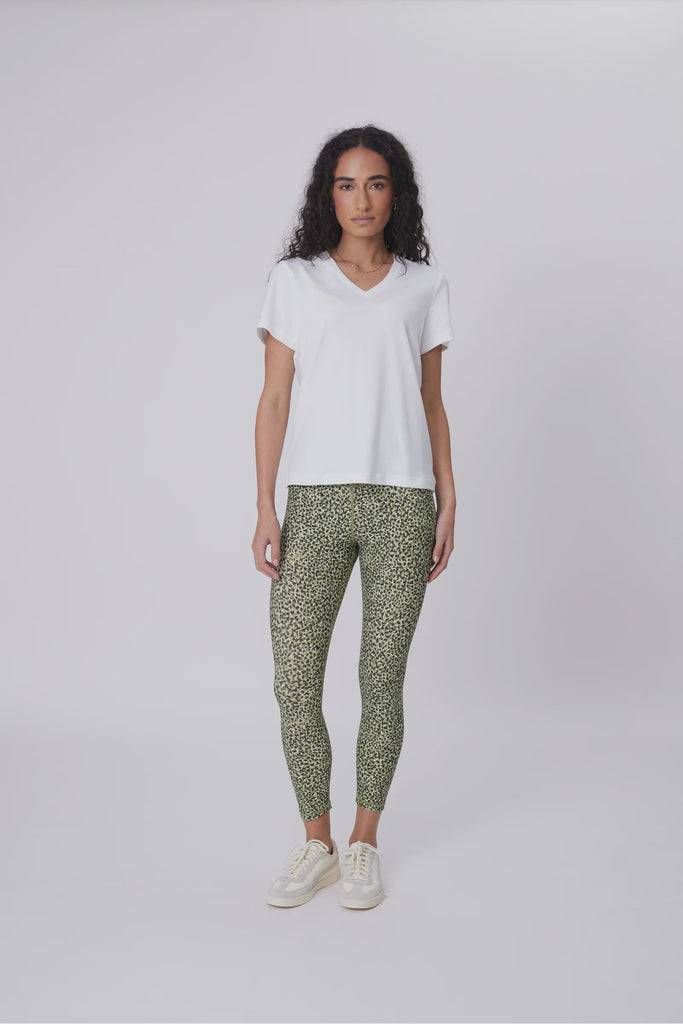 Woman wearing a white t-shirt and green patterned leggings on a plain background. Marlow Pace 7.8 Legging in Green Willow Print.