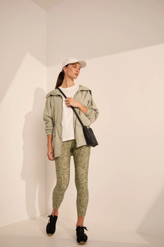 Woman wearing a white t-shirt and green patterned leggings on a plain background. Marlow Pace 7.8 Legging in Green Willow Print.