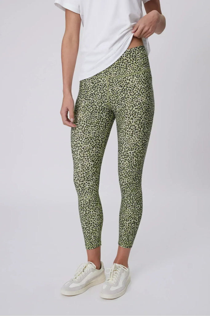 Woman wearing a white t-shirt and green patterned leggings on a plain background. Marlow Pace 7.8 Legging in Green Willow Print.