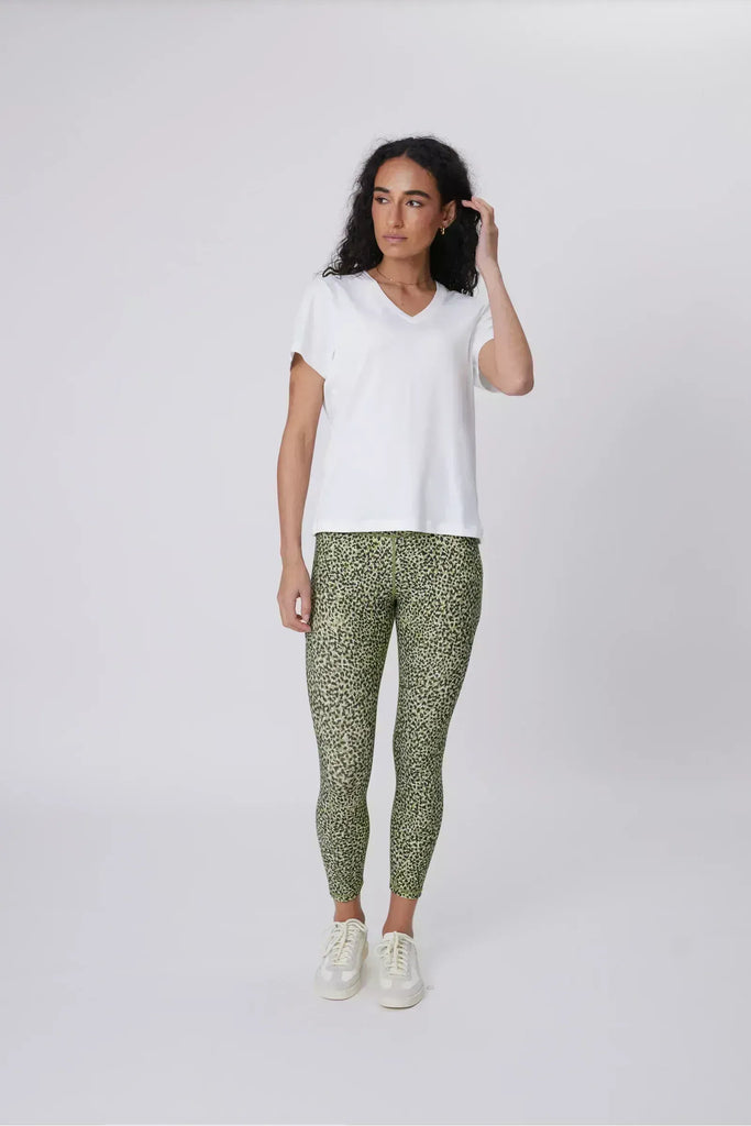 Woman wearing a white t-shirt and green patterned leggings on a plain background. Marlow Pace 7.8 Legging in Green Willow Print.