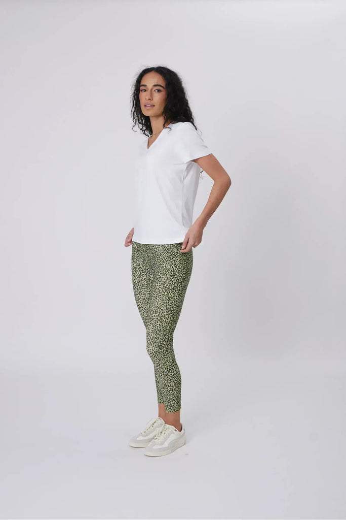 Woman wearing a white t-shirt and green patterned leggings on a plain background. Marlow Pace 7.8 Legging in Green Willow Print.