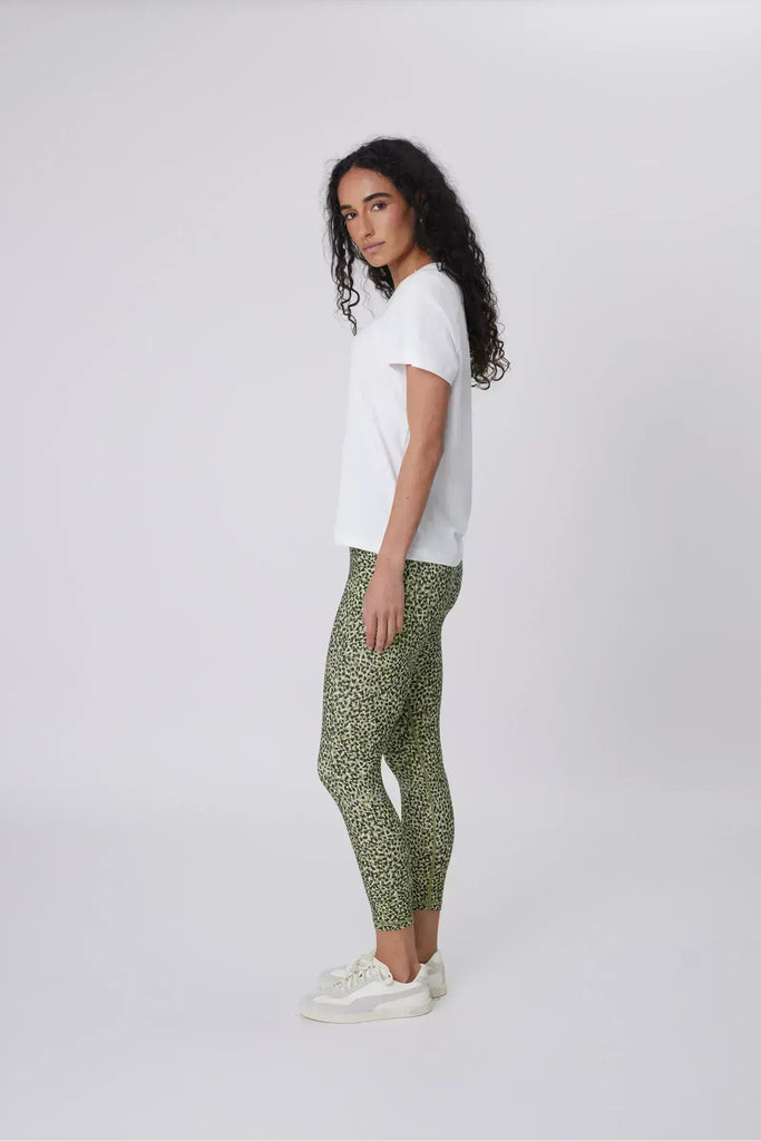Woman wearing a white t-shirt and green patterned leggings on a plain background. Marlow Pace 7.8 Legging in Green Willow Print.