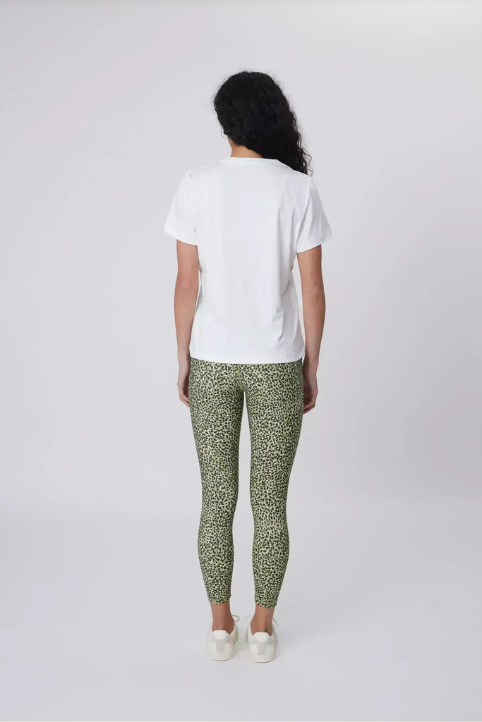 Woman wearing a white t-shirt and green patterned leggings on a plain background. Marlow Pace 7.8 Legging in Green Willow Print.
