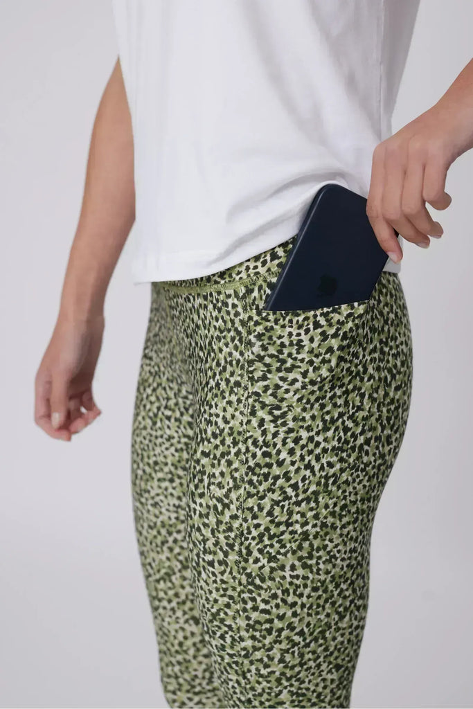 Woman wearing a white t-shirt and green patterned leggings on a plain background. Marlow Pace 7.8 Legging in Green Willow Print.