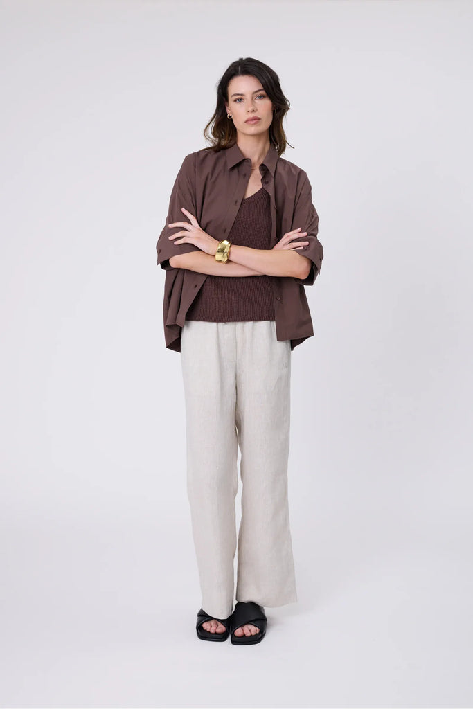 Woman wearing a chocolate brown knit tee, shirt and ecru pant on a grey background. Marlow Wisp knit Tee Carob.