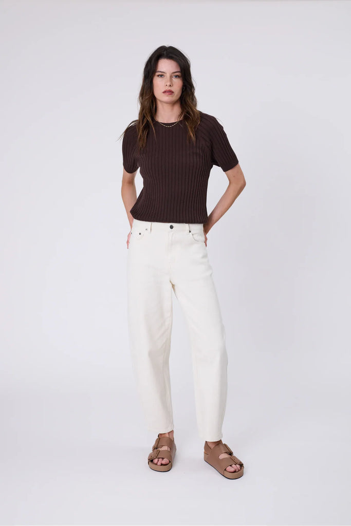 Woman wearing a chocolate brown knit tee and ecru pant on a grey background. Marlow Wisp knit Tee Carob.