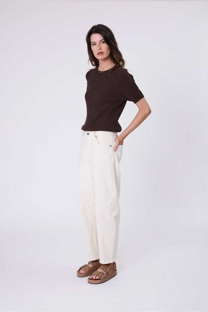 Woman wearing a chocolate brown knit tee and ecru jean on a grey background. Marlow Wisp knit Tee Carob.