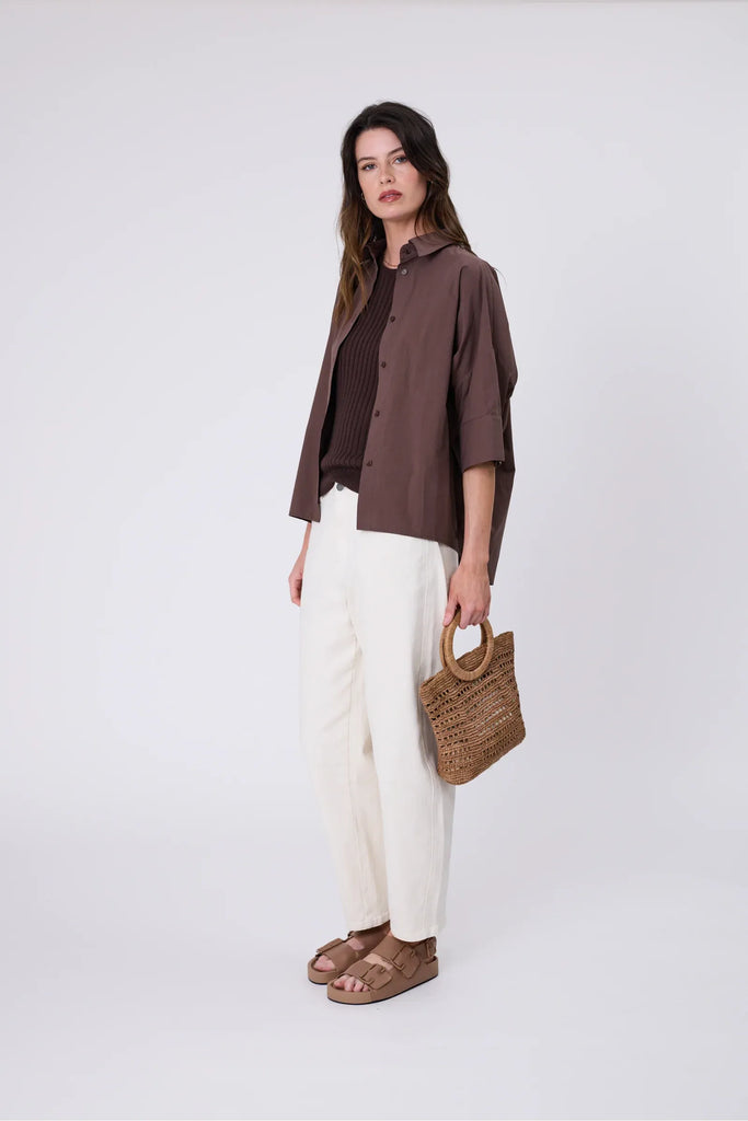 Woman wearing a chocolate brown knit tee, shirt and ecru jean on a grey background. Marlow Wisp knit Tee Carob.