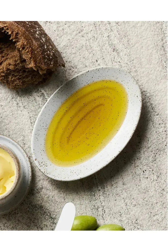 Robert Gordon Garden to Table Oil Dish filled with oil sitting alongside spreadable butter, bread, and green apples on a textured surface.