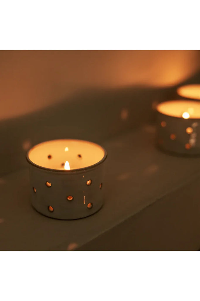 Two lit candles in decorative holders on a reflective surface with a warm glow.
